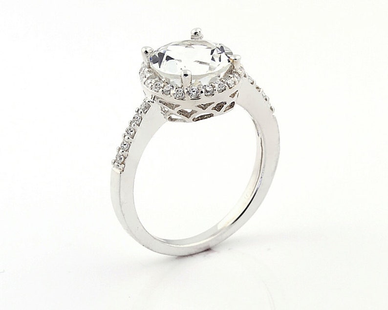May include: A silver ring with a large, clear, round gemstone surrounded by a halo of smaller gemstones. The band is set with smaller gemstones.