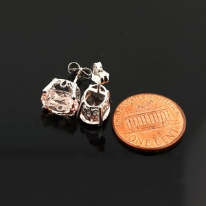 K&ouml;nnte beinhalten: Ein Paar silberne Ohrringe mit einem rosafarbenen ovalen Edelstein in jedem Ohrring. Die Ohrringe werden neben einem US-Cent zur Gr&ouml;&szlig;envergleich gezeigt.