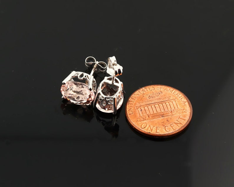 K&ouml;nnte beinhalten: Ein Paar silberne Ohrringe mit einem rosafarbenen ovalen Edelstein in jedem Ohrring. Die Ohrringe werden neben einem US-Cent zur Gr&ouml;&szlig;envergleich gezeigt.