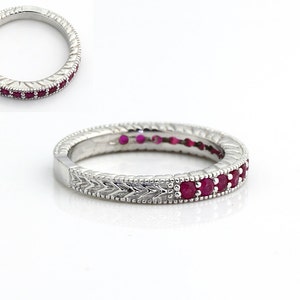 May include: A silver band ring with a row of red ruby stones set in the center of the band. The band has a decorative, textured design.