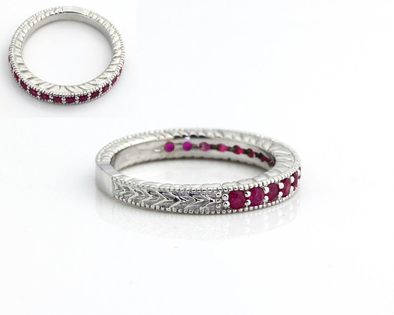 May include: A silver band ring with a row of red ruby stones set in the center of the band. The band has a decorative, textured design.