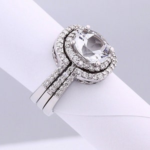May include: A silver ring set with a large, clear oval-shaped gemstone surrounded by a double halo of smaller, sparkling gemstones.