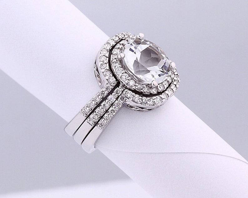 May include: A silver ring set with a large, clear oval-shaped gemstone surrounded by a double halo of smaller, sparkling gemstones.