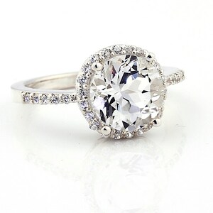 May include: A silver ring with a large, clear, round gemstone surrounded by a halo of smaller gemstones.