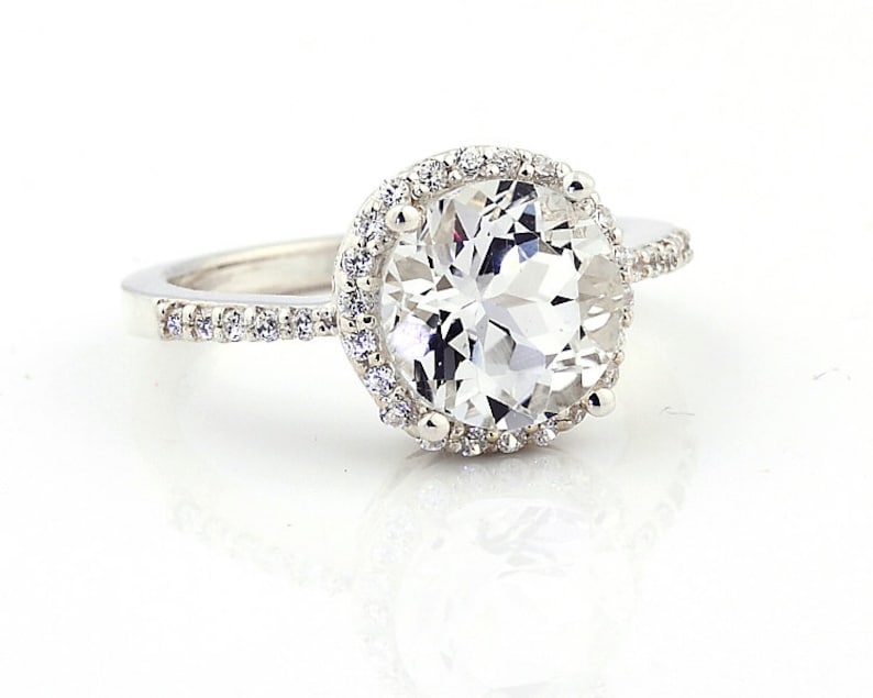 May include: A silver ring with a large, clear, round gemstone surrounded by a halo of smaller gemstones.