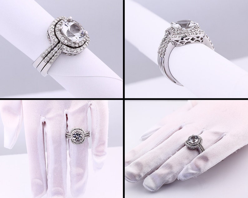 May include: A silver engagement ring set with a large, clear, oval-shaped center stone surrounded by smaller stones. The ring is on a white background.