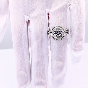May include: A silver engagement ring with a large, round, clear center stone surrounded by smaller stones. The ring has a double band with smaller stones.