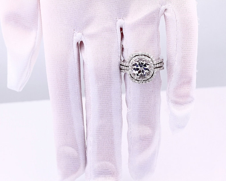 May include: A silver engagement ring with a large, round, clear center stone surrounded by smaller stones. The ring has a double band with smaller stones.