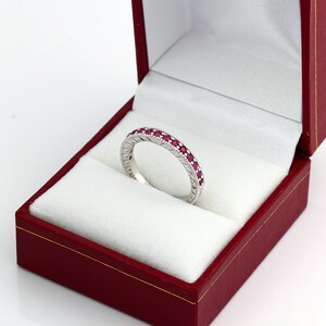 May include: A white gold band ring with a row of ruby gemstones set in the band.