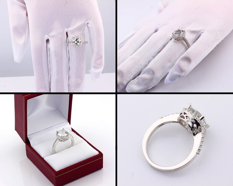 May include: A silver engagement ring with a large, round, clear center stone surrounded by smaller stones. The ring is on a white background.