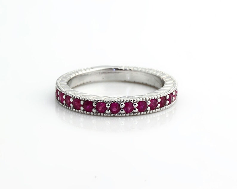 May include: A silver band ring with a row of small, red ruby stones set in the center.