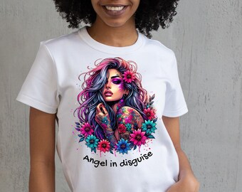 May include: White t-shirt featuring a colorful illustration of a woman with floral accents, tattoos, and the text "Angel in disguise." The artwork includes pink, purple, blue, and teal hues. The shirt is a casual, everyday wear item.