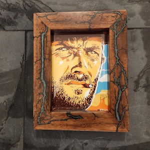 May include: Framed print featuring a stylized portrait of a man with a beard and a cigar, set against a desert landscape. The wooden frame has a unique design with a tree-like pattern and teal accents.