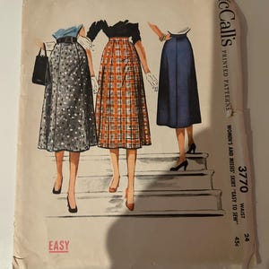 以下が含まれることがあります： スカート用ヴィンテージMcCall'sプリントパターン封筒、番号3770。グレーの柄物スカート、オレンジのチェック柄スカート、無地のブルースカートの3種類のイラストが描かれています。テキストにはEASY、McCall's、3770と記載されています。