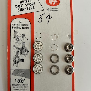 May include: A package of four Dritz Dot Sport Snappers, No. 609/6 Golfing, featuring silver-toned metal fasteners with a golf club graphic. The white and orange cardboard backing displays illustrations of golfing, fishing, bowling, and boating activities.