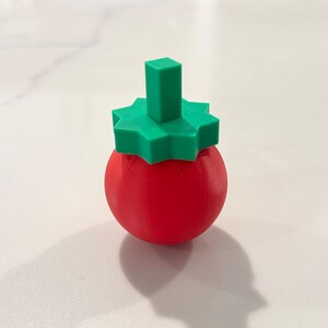 Op de afbeelding: Een rood, bolvormig object met een groene, stervormige bovenkant en een rechthoekige steel. Het object is waarschijnlijk een decoratief item of een unieke flesstopper, tegen een witte achtergrond. 3D-geprint.
