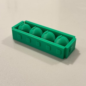 Op de afbeelding: Een groene 3D-geprinte container met vier groene bolvormige objecten. De container is rechthoekig met afgeronde hoeken en vierkante uitsparingen. De bollen hebben een getextureerd, gelaagd uiterlijk.