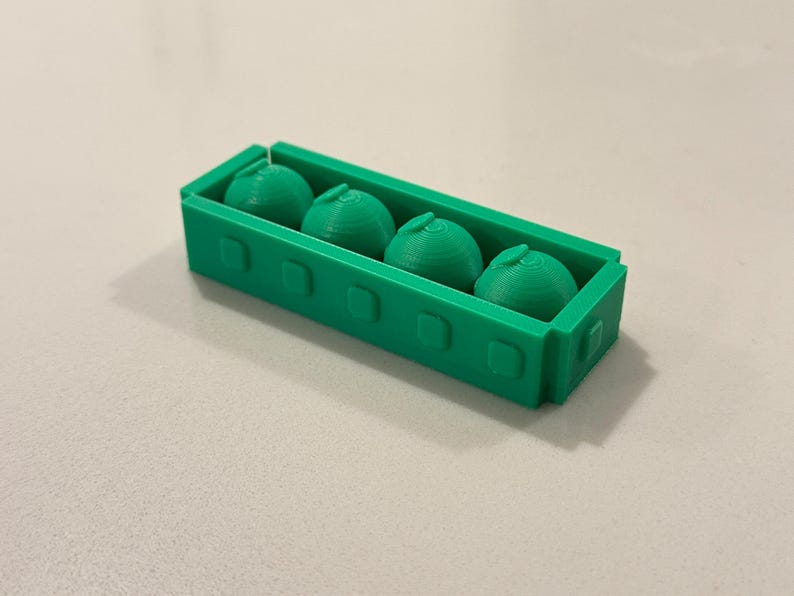 Op de afbeelding: Een groene 3D-geprinte container met vier groene bolvormige objecten. De container is rechthoekig met afgeronde hoeken en vierkante uitsparingen. De bollen hebben een getextureerd, gelaagd uiterlijk.