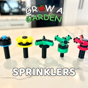 May include: A collection of five colorful sprinklers with black stems. The sprinklers have various designs, including a blue and black top, a yellow gear-shaped top, and green and red tops. The text "GROW A GARDEN" and "SPRINKLERS" are displayed.