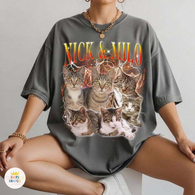 May include: Gray t-shirt featuring a graphic of six cats with the text "NICK & MILO" in a retro font. The cats are in various poses, with a lightning bolt design in the background. The shirt is a casual, oversized style.