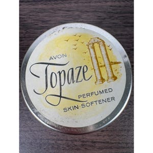 Puede incluir: Lata vintage de suavizante de piel perfumado Topaze de Avon. La lata redonda presenta la palabra "Topaze" en cursiva, con "Avon" arriba y "Perfumed Skin Softener" abajo. El diseño incluye un fondo amarillo con una ilustración de columna clásica.