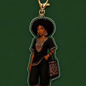 May include: An acrylic keychain featuring a character with dark skin and voluminous curly hair, wearing a black tunic and pants with gold geometric patterns. The character holds a matching black tote bag with gold designs and wears gold hoop earrings.