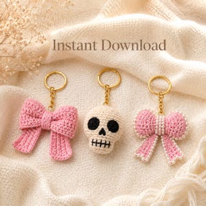 Può includere: Tre portachiavi all'uncinetto che includono un fiocco rosa, un teschio color crema con occhi e bocca ricamati in nero, e un fiocco rosa decorato con perle bianche. Ogni articolo include un anello e una catena in metallo dorato. Testo: Instant Download.