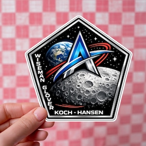 May include: A sticker with a space exploration theme. The design includes a blue and silver letter "A", a depiction of the moon and Earth, and the text "WISEMAN GLOVER" and "KOCH - HANSEN" against a black background.