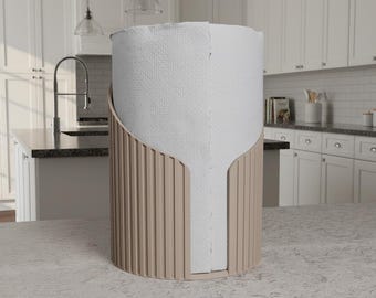 May include: A beige paper towel holder with vertical grooves, holding a roll of white paper towels. The holder has a curved design and is placed on a countertop in a kitchen setting.