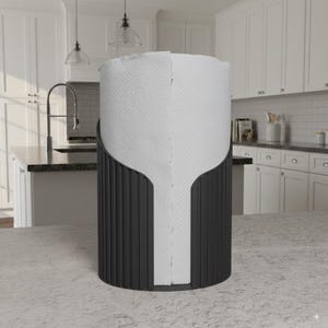 Puede incluir: Un soporte negro para toallas de papel con un diseño vertical, que sostiene un rollo de toallas de papel blancas. El soporte tiene una abertura curva para facilitar el acceso a las toallas de papel. El accesorio de cocina está sobre una encimera.