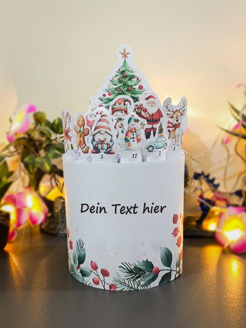 May include: A white Christmas advent calendar with a festive design. The top features a Christmas tree, Santa Claus, and other holiday characters. The base has the text "Dein Text hier" and is decorated with holly and berries.