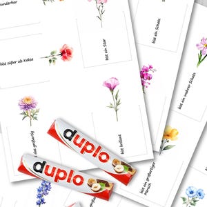 Puede incluir: Una colecci&oacute;n de tarjetas blancas con ilustraciones florales en acuarela y texto en alem&aacute;n, junto con varias barras de chocolate Duplo rojas y blancas. Las tarjetas presentan varias flores y frases como "bist ein Schatz."