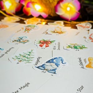 Puede incluir: Una colecci&oacute;n de pegatinas y tarjetas ilustradas con tem&aacute;tica navide&ntilde;a. Las pegatinas presentan dise&ntilde;os festivos como un gnomo, un &aacute;rbol de Navidad y regalos. Las tarjetas tienen frases como "Eres una estrella" y "Lleno de magia".