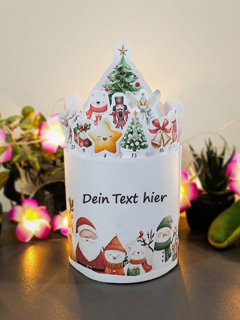 May include: A white Christmas advent calendar with a cylindrical base and a decorative top. The base features Santa Claus, snowmen, and polar bears. The top has cutouts of Christmas trees, stars, and other festive elements. The text "Dein Text hier" is printed on the base.