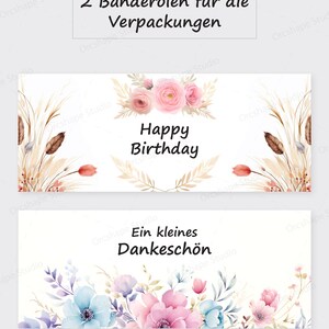 Puede incluir: Dos bandas de papel decorativas con dise&ntilde;os florales. Una banda dice "Happy Birthday" con rosas rosas y detalles beige. La otra dice "Ein kleines Dankesch&ouml;n" con flores azules y rosas.