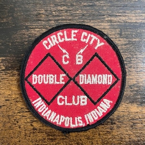 Könnte beinhalten: Ein runder, roter Aufnäher mit weißem Text. Der Text lautet "CIRCLE CITY" oben, "DOUBLE DIAMOND CLUB" in der Mitte und "INDIANAPOLIS, INDIANA" unten. Zwei schwarze Diamanten befinden sich in der Mitte.