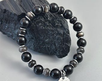 May include: Black beaded bracelet with silver accents and a small, round, silver charm. The bracelet features large, round, black beads interspersed with smaller, silver-colored beads. The charm is engraved with the word "Yzen" in a script font.