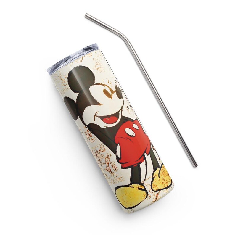 May include: A cylindrical tumbler featuring a graphic of Mickey Mouse with black ears, a red pair of shorts, and yellow shoes against a cream-colored background with faint sketches. A clear plastic lid is attached, and a bent metal straw is included.