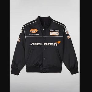 Op de afbeelding: Zwarte satijnen bomberjack met witte en oranje race-patches. Voorzien van het McLaren-logo in het wit over de borst. Inclusief een knoopsluiting, zwarte geribde manchetten en een witte streep.