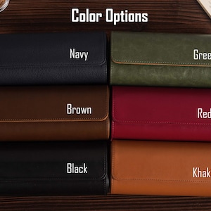 Pu&ograve; includere: Un assortimento di custodie per orologi in pelle in vari colori, tra cui blu navy, verde, marrone, rosso, nero e kaki. Ogni custodia &egrave; rettangolare con chiusura a patta ed &egrave; etichettata con il suo colore. Il testo "Color Options" &egrave; in alto.