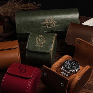 Pu&ograve; includere: Un assortimento di custodie per orologi in pelle in vari colori, tra cui verde, marrone e rosso. Alcune custodie sono personalizzate con nomi e iniziali. Un orologio argentato con quadrante nero &egrave; esposto in una custodia marrone aperta.