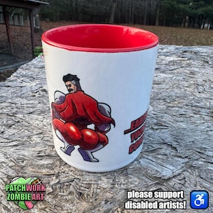 以下が含まれることがあります： 赤い内側の白いセラミックマグ。赤いマントを着た筋肉質なキャラクターの漫画イラストが特徴です。マグには「...EARTH...YOU...CON...」と「please support disabled artists!」と書かれています。