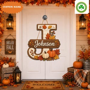 May include: A decorative wooden door sign shaped like the letter J, featuring a white wood-plank background, the name Johnson in white script, and an arrangement of orange pumpkins, autumn leaves, and berries in shades of red, gold, and brown.