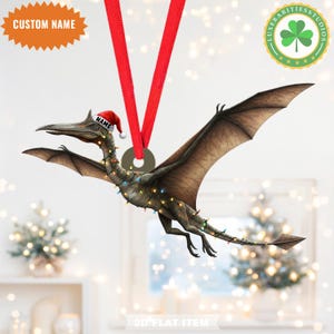 May include: A Pterodactyl Christmas ornament with a Santa hat and string lights. The ornament hangs from a red ribbon and features the text "NAME" on the hat and "CUSTOM NAME" on a starburst. The ornament is a 2D flat item.