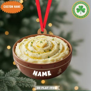 May include: A round, brown ornament featuring a bowl of mashed potatoes topped with butter and herbs. The ornament has a red ribbon for hanging and includes the text "NAME" and "CUSTOM NAME". The ornament is a 2D flat item.