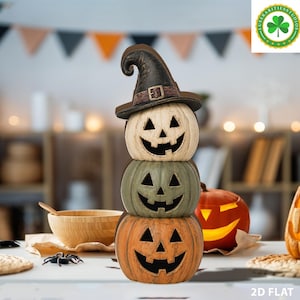 Könnte beinhalten: Ein vertikaler Stapel aus drei geschnitzten Kürbissen mit ausgeschnittenen Jack-o'-Lantern-Gesichtern. Der oberste Kürbis ist cremefarben und trägt einen schwarzen Hexenhut mit brauner Schnalle. Der mittlere Kürbis ist salbeigrün, der untere orange.
