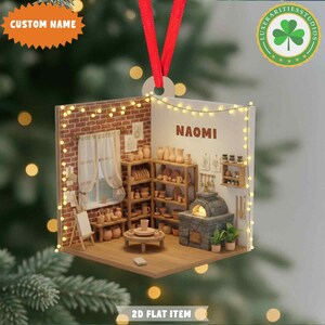 May include: A personalized ornament featuring a miniature pottery studio scene. The ornament includes a brick wall, shelves filled with pottery, and the name "NAOMI". The ornament is a 2D flat item with a red ribbon for hanging.