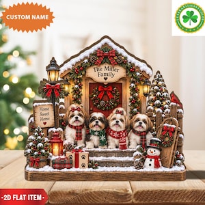 Può includere: Un cartello decorativo piatto 2D raffigurante quattro cani Shih Tzu seduti sui gradini di un portico davanti a una porta. La scena include una ghirlanda natalizia, un cartello con scritto The Miller Family, un cartello Home Sweet Home, un pupazzo di neve e regali.