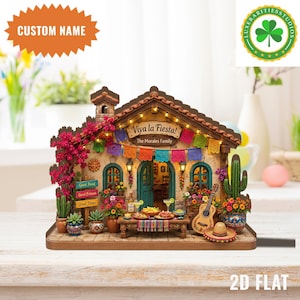 May include: A miniature, detailed diorama of a festive Mexican restaurant, featuring a sign that reads "Viva la Fiesta!" and "The Morales Family." The scene includes a guitar, sombrero, and a table laden with food and drinks. Colorful flags and flowers decorate the building.