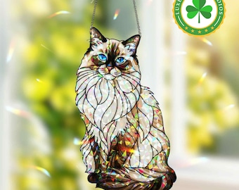 May include: A stained glass cat suncatcher with a chain for hanging. The cat has blue eyes, a fluffy white and brown coat, and is sitting upright. The suncatcher has a colorful, iridescent finish. The logo "LUXERARITIESTUDIOS" is in the upper right corner.